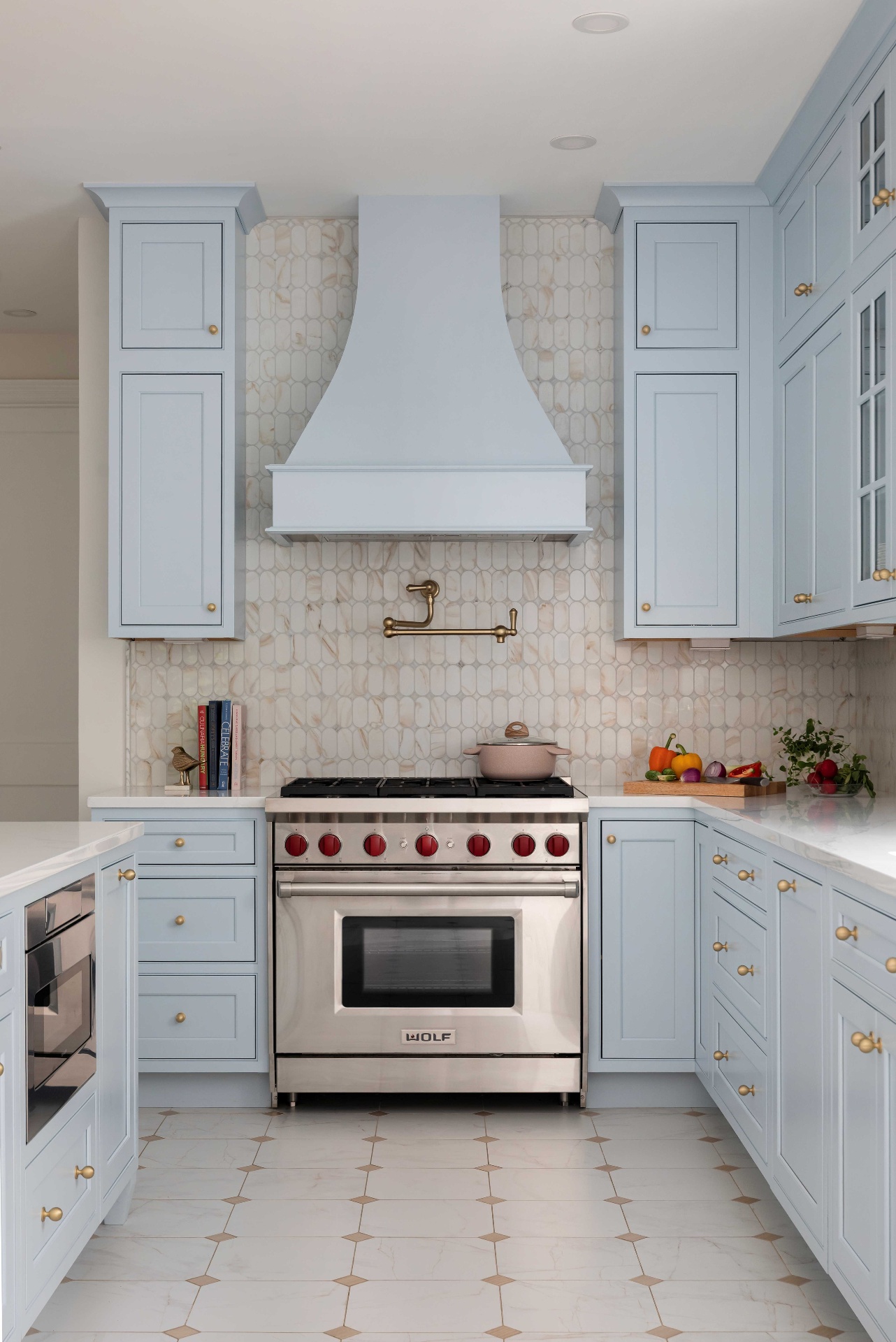 Wolf range with red knobs flanked by tall Moonmist cabinets and elongated marble mosaic