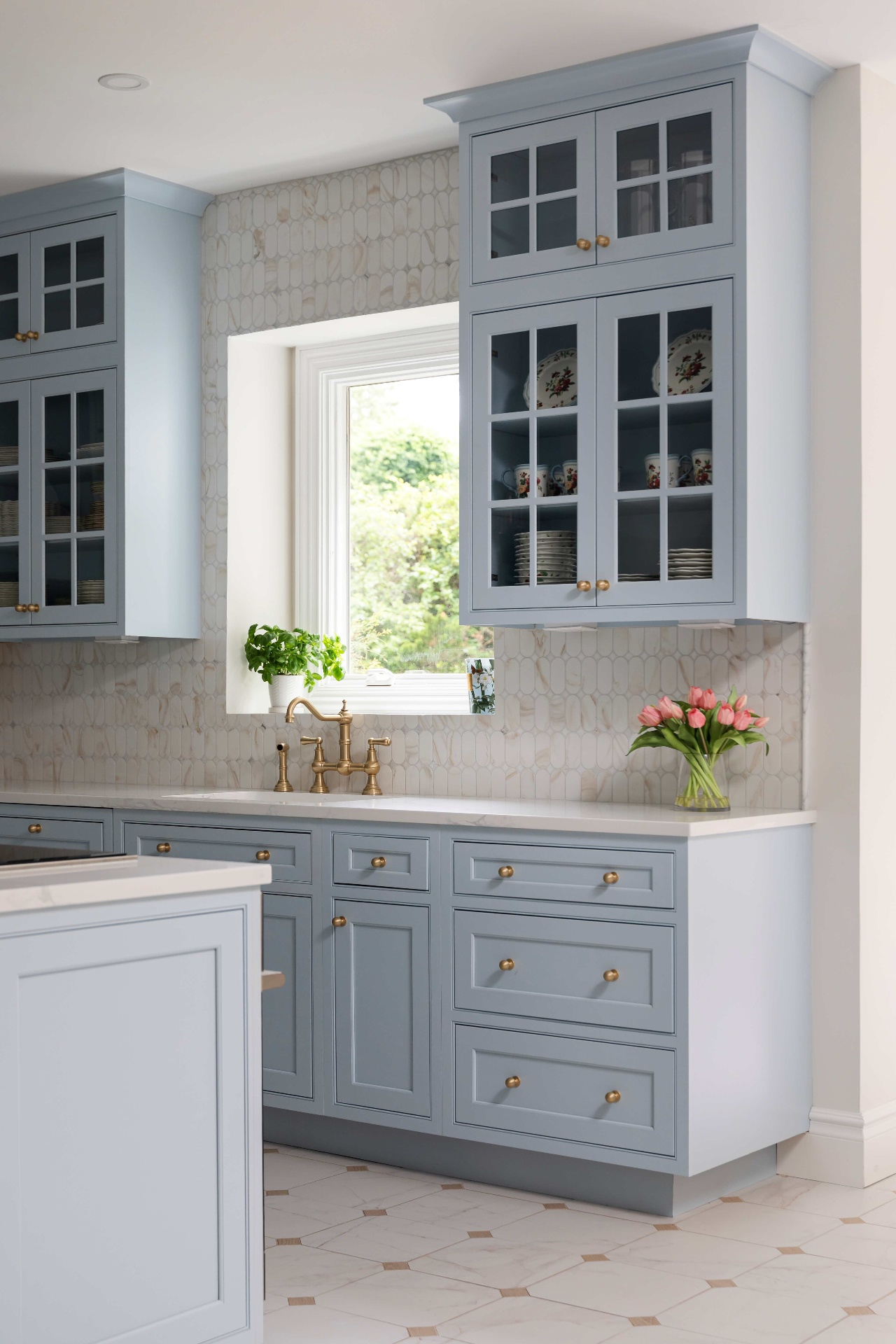 Window sink with brass faucet, tulips, and stacked glass-front upper cabinets