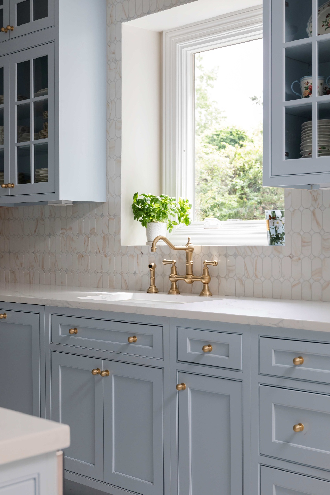 Brass bridge faucet at a window over an undermount sink with inset Moonmist cabinetry