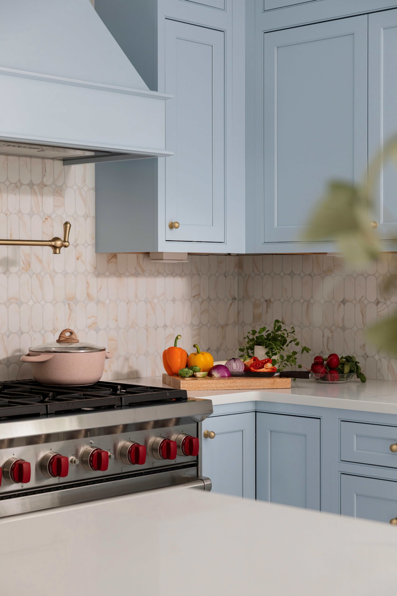 Close-up of the Wolf range knobs, brass pot filler and marble mosaic backsplash